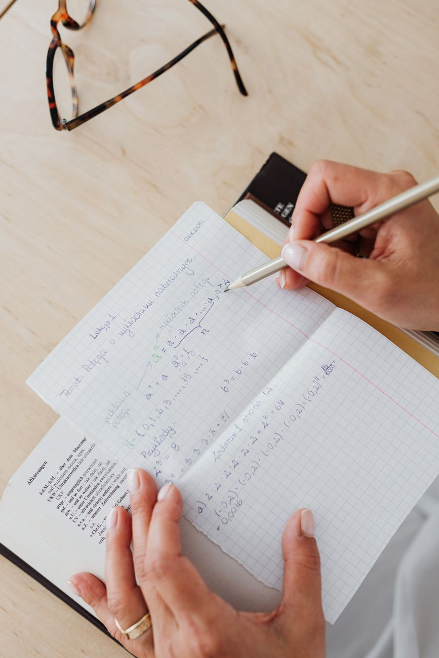 Notebook page on a sunlit desk showing two contrasting weight-loss curves — a steep straight line labelled '3,500 rule' and a flattening curve labelled 'Hall model' — beside a glass of water and a calculator