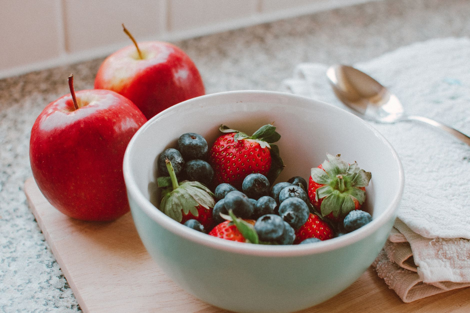 Fresh whole fruit and a glass of water on a kitchen counter as lower-sugar swaps for sweetened drinks and snacks