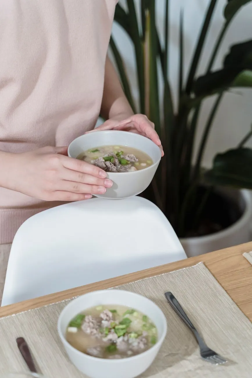 A person holding a bowl of soup beside a set dining table