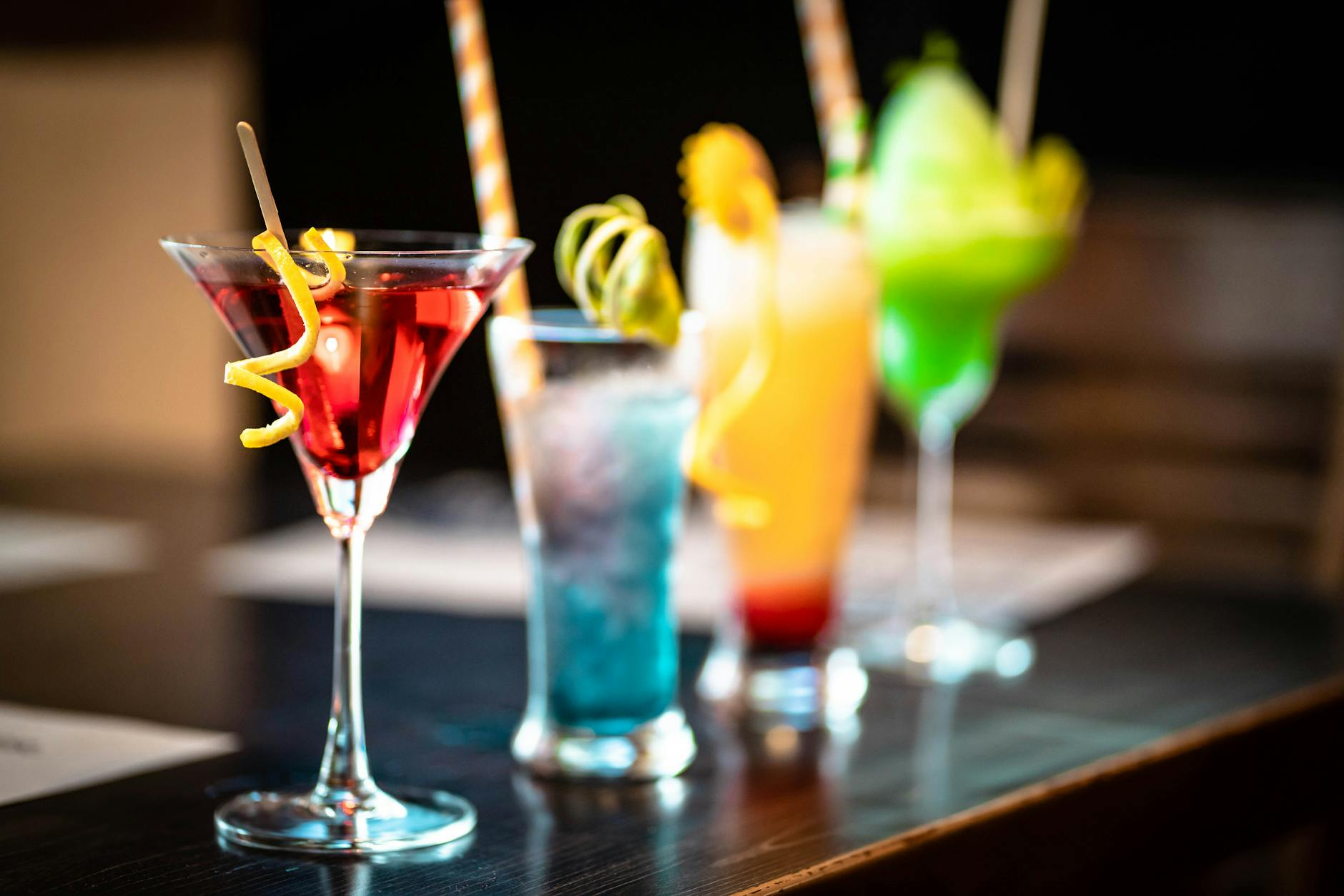 Glasses of wine, beer, and spirits arranged on a wooden bar counter alongside fresh lemon, lime, and a small notepad for tracking