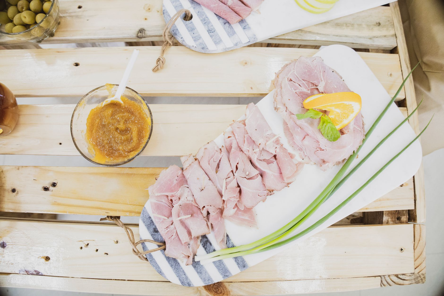 Australian Christmas lunch spread on a sunlit outdoor table — a glazed leg ham, a platter of cooked king prawns on ice, sliced roast turkey, mixed salads, and a pavlova with strawberries and cream beside a glass of sparkling wine