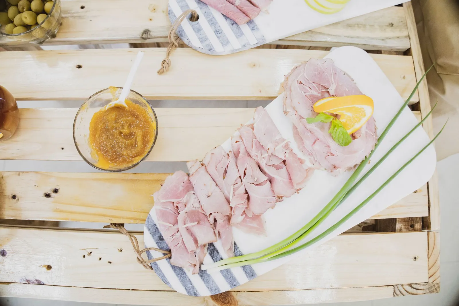 Australian Christmas lunch spread on a sunlit outdoor table — a glazed leg ham, a platter of cooked king prawns on ice, sliced roast turkey, mixed salads, and a pavlova with strawberries and cream beside a glass of sparkling wine