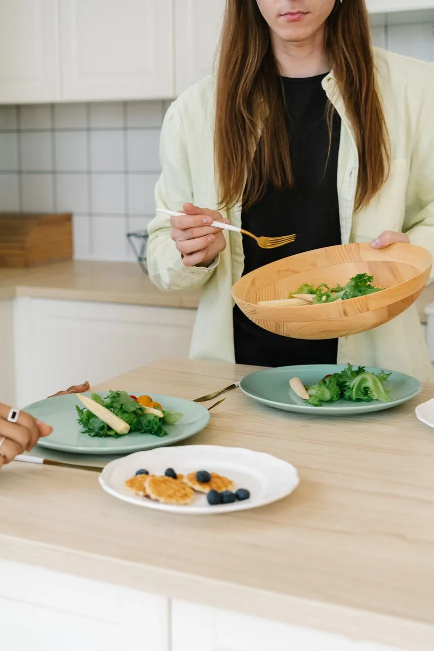 A person serving salad from a wooden bowl at a dining table