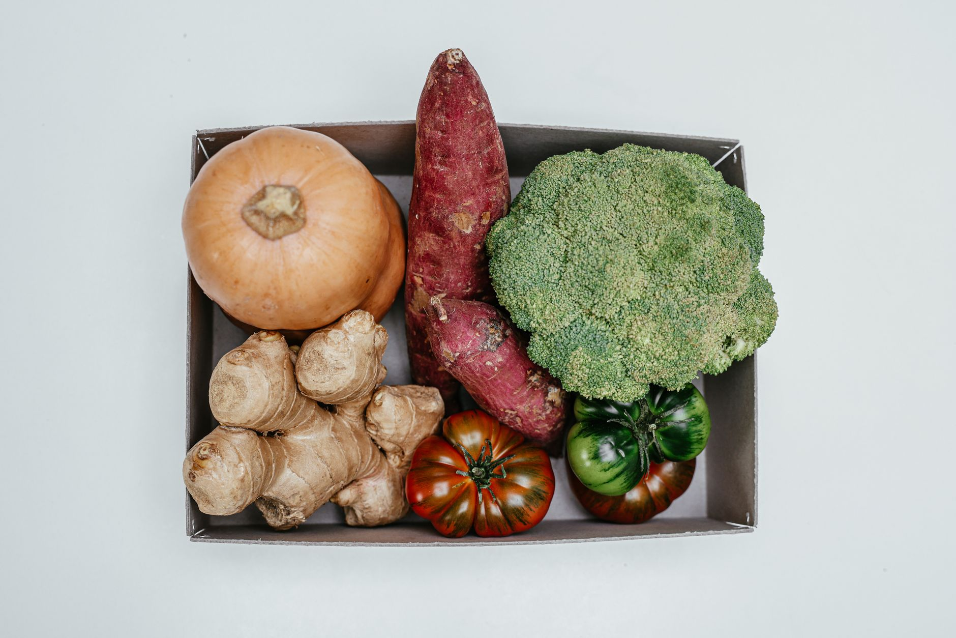Fresh Australian vegetables — broccoli florets, baby spinach, zucchini, sweet potato, and tomatoes — on a sunlit kitchen counter beside a digital scale, a smartphone showing a calorie tracking app, and a notepad with kilojoule numbers