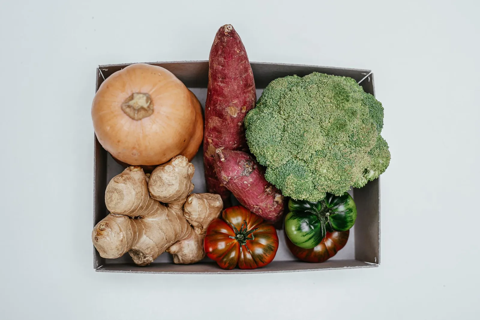 Fresh Australian vegetables — broccoli florets, baby spinach, zucchini, sweet potato, and tomatoes — on a sunlit kitchen counter beside a digital scale, a smartphone showing a calorie tracking app, and a notepad with kilojoule numbers