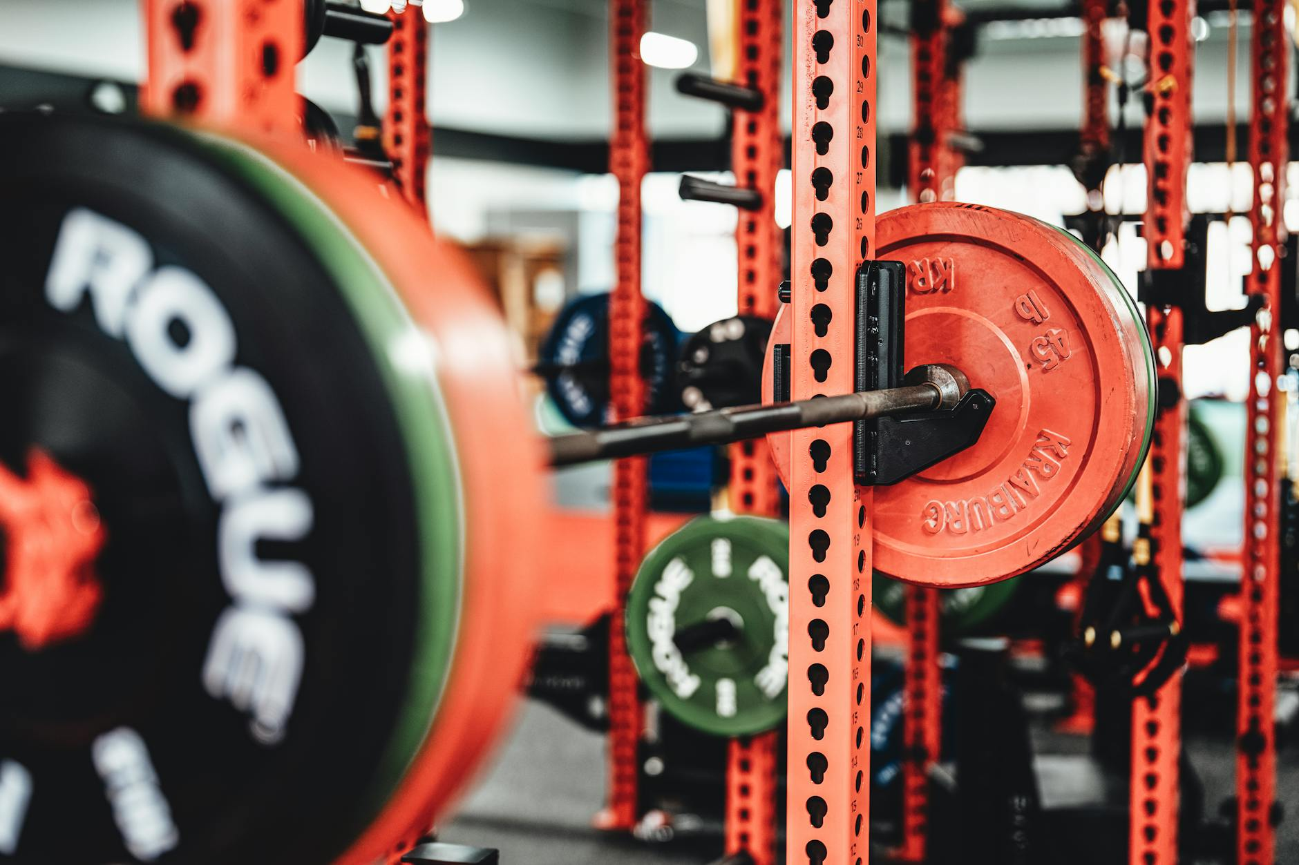 Person performing a barbell back squat in a bright modern gym with weight plates and a fitness watch on a nearby bench