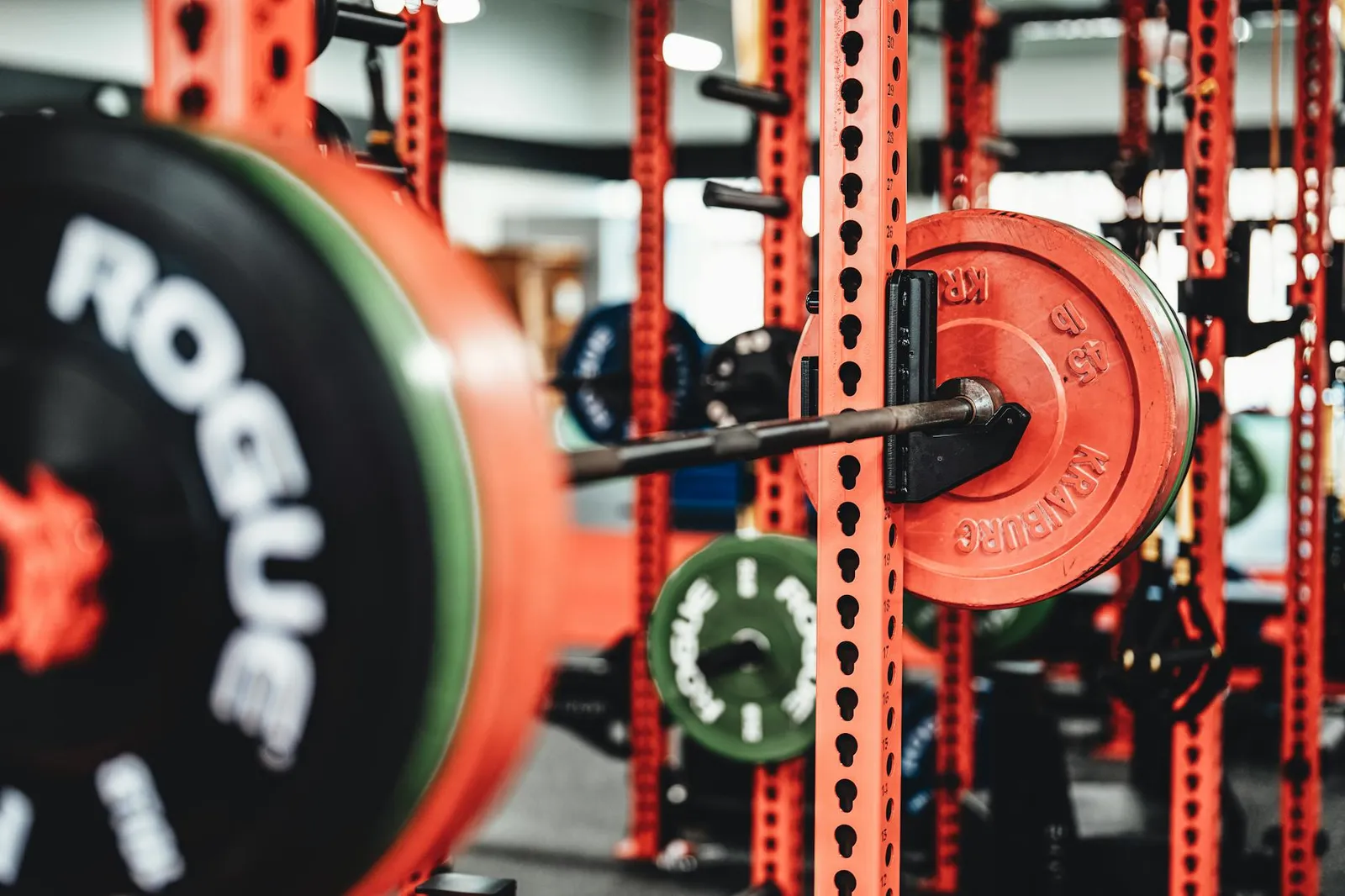 Person performing a barbell back squat in a bright modern gym with weight plates and a fitness watch on a nearby bench