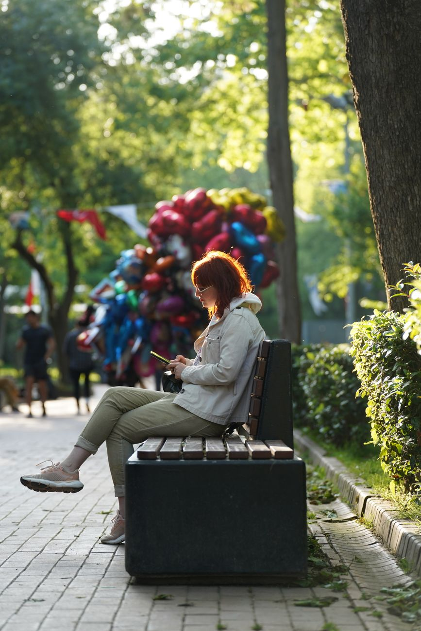 A person walking outdoors on a sunlit path beside a smartphone displaying a continuous glucose monitor app graph showing postprandial glucose curve and a printed nutrition information panel on a wooden park bench