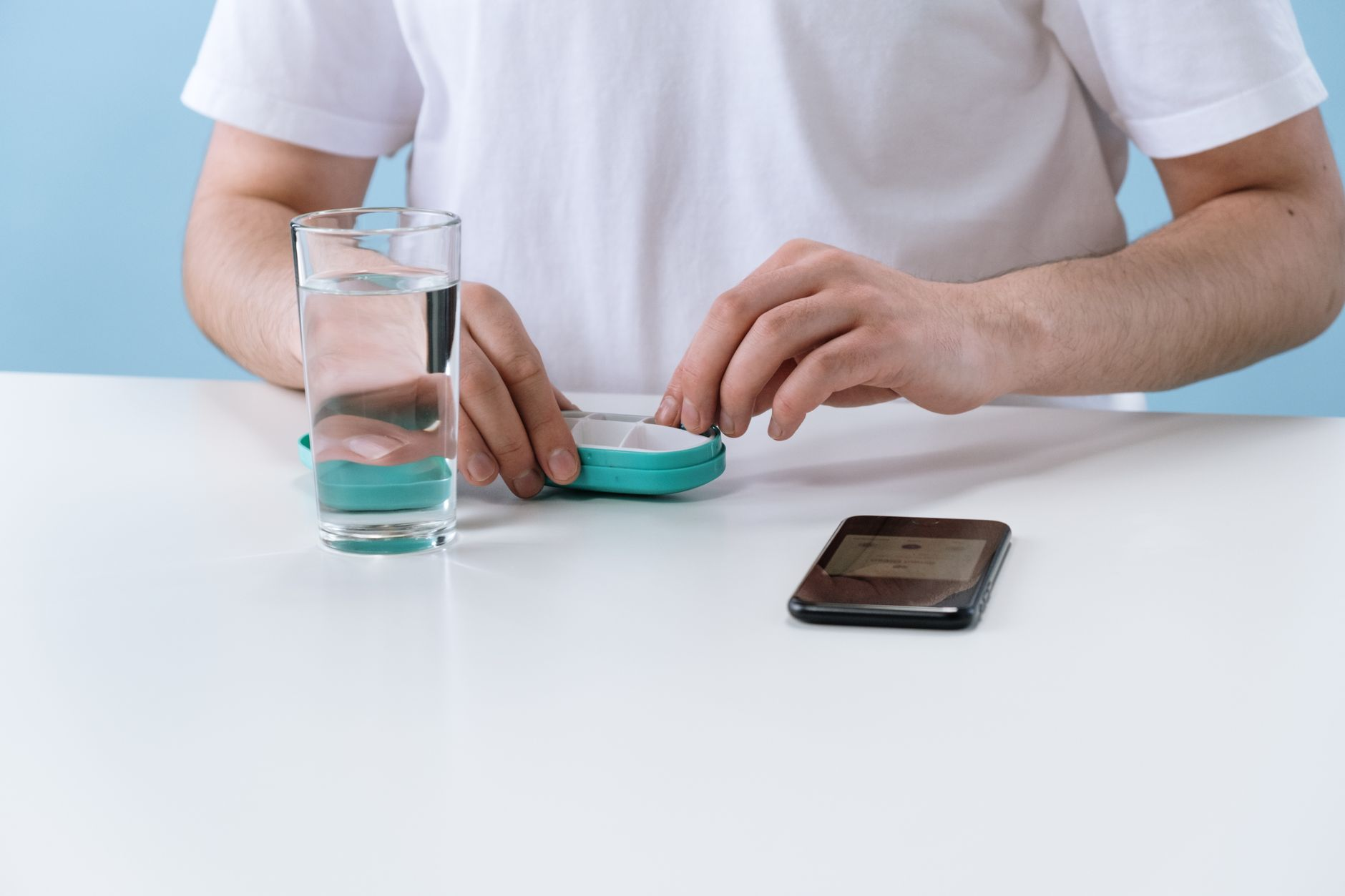 A creatine supplement tub with a scoop of white powder beside a bathroom scale, a glass of water, and a smartphone showing a weight-trend graph on a sunlit bathroom floor, illustrating the water weight the scale adds when creatine supplementation starts