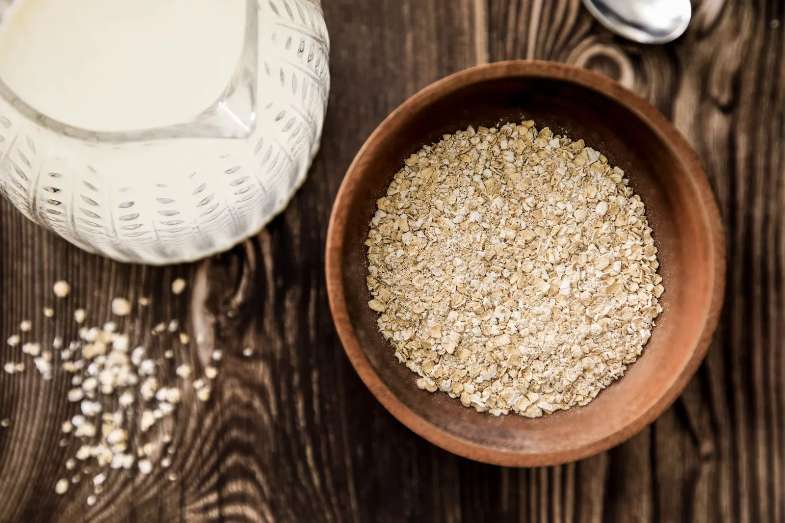 A wooden bowl of oats beside a glass jug of milk