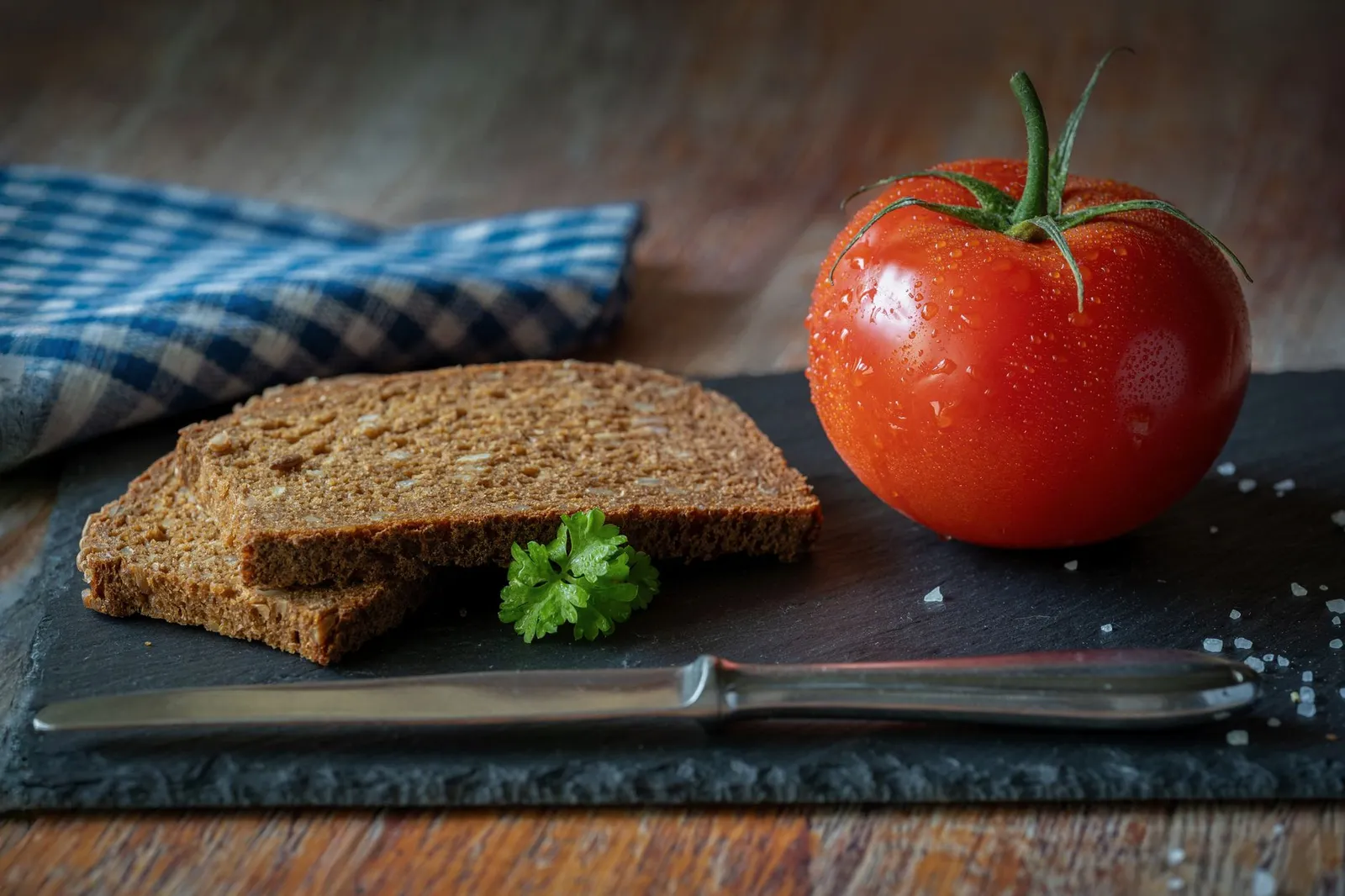 Slices of brown bread beside a tomato and parsley on a slate board