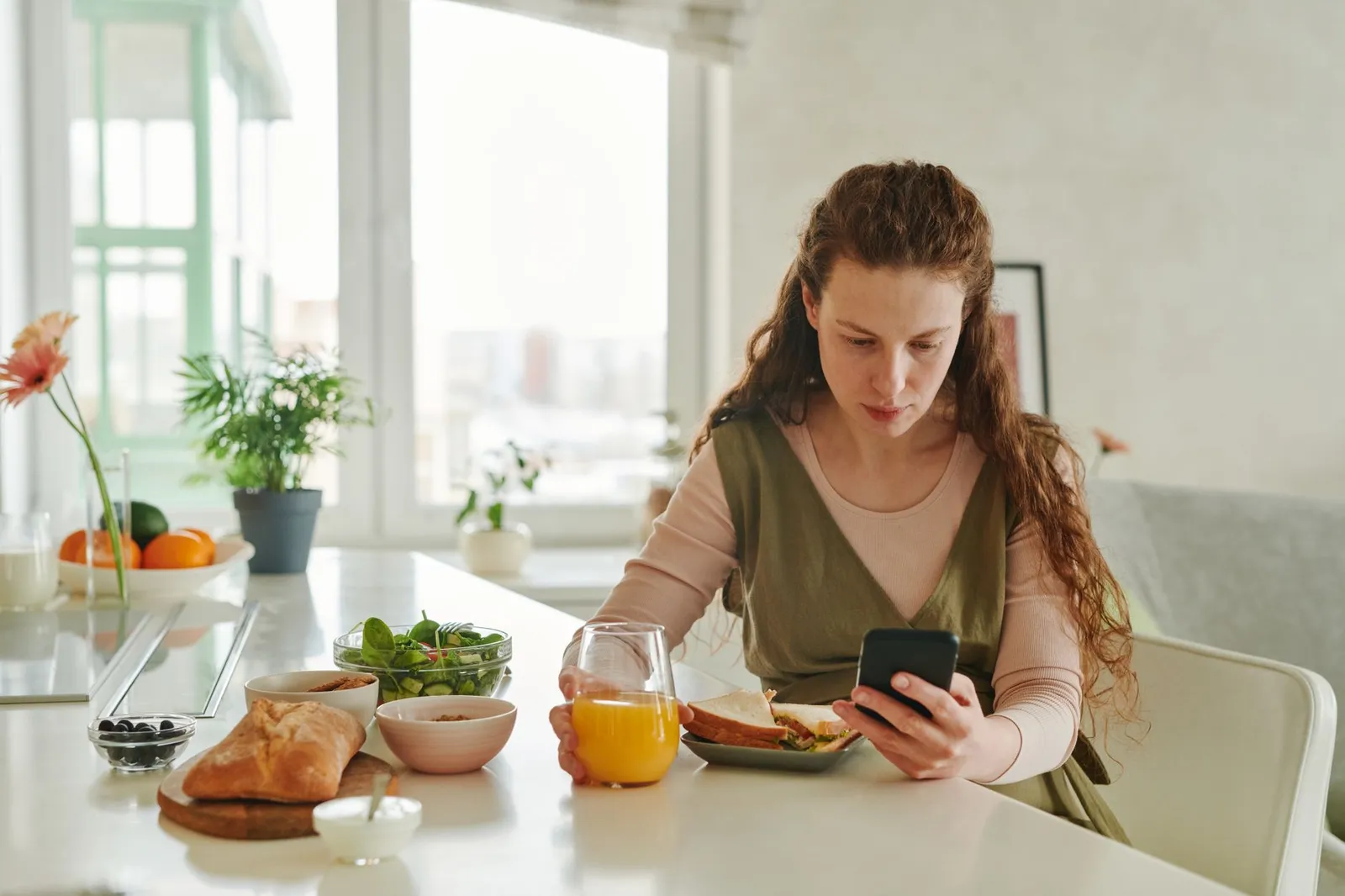 An older adult and a younger adult sharing a healthy meal at a sunlit kitchen table beside a smartphone showing a calorie tracking app and a printed energy-expenditure chart, illustrating that size-adjusted daily calorie burn stays stable from age 20 to 60