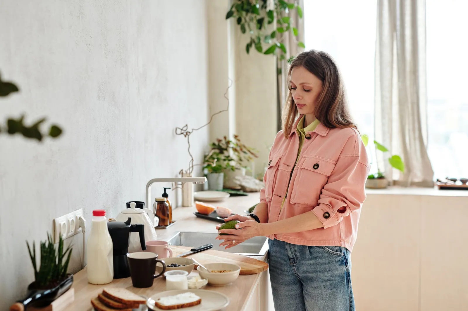 A kitchen scale, a smartphone showing a calorie tracking app, a bottle of cooking oil, and a cup of coffee with milk on a sunlit kitchen counter, illustrating the hidden calories that make a 1,200-calorie log read lower than actual intake