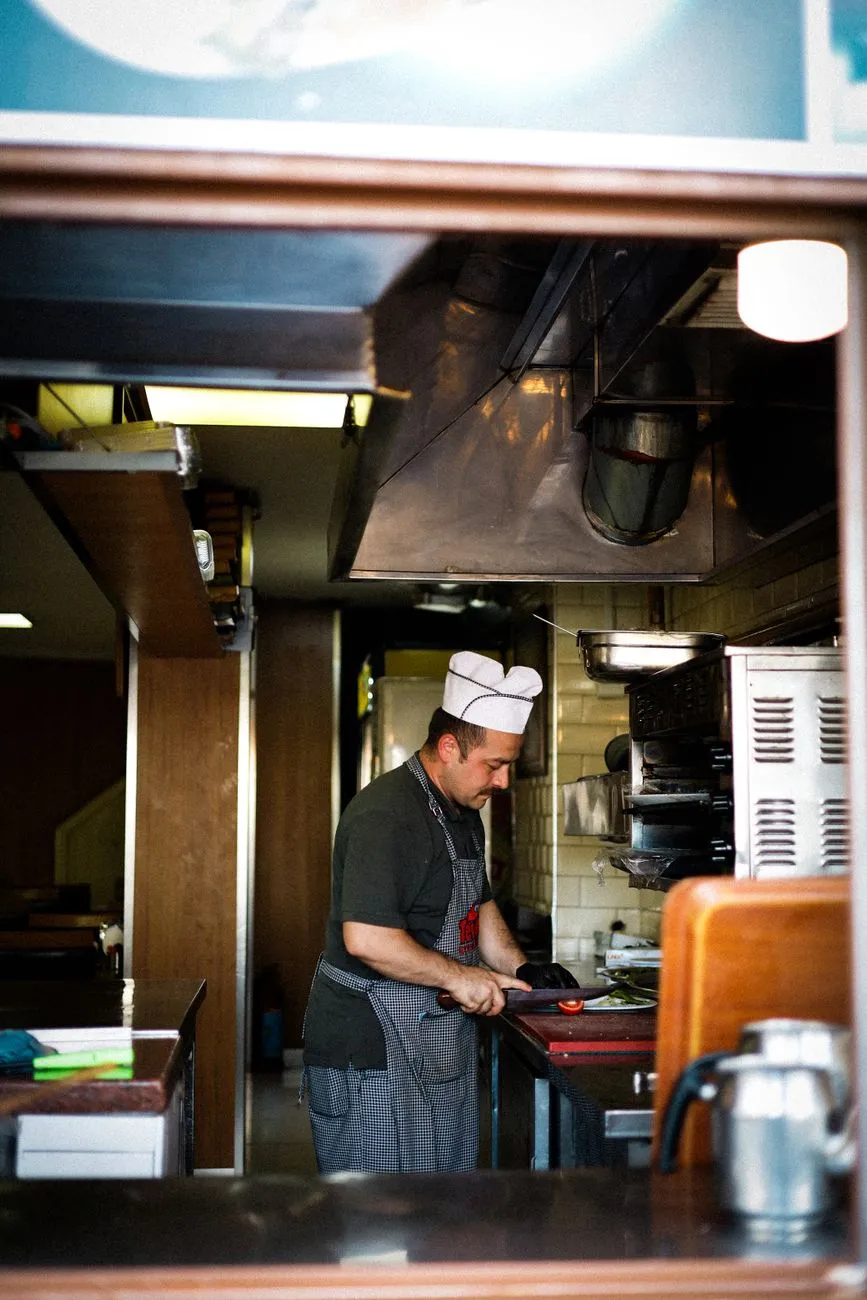 A cook slicing a tomato in a restaurant kitchen