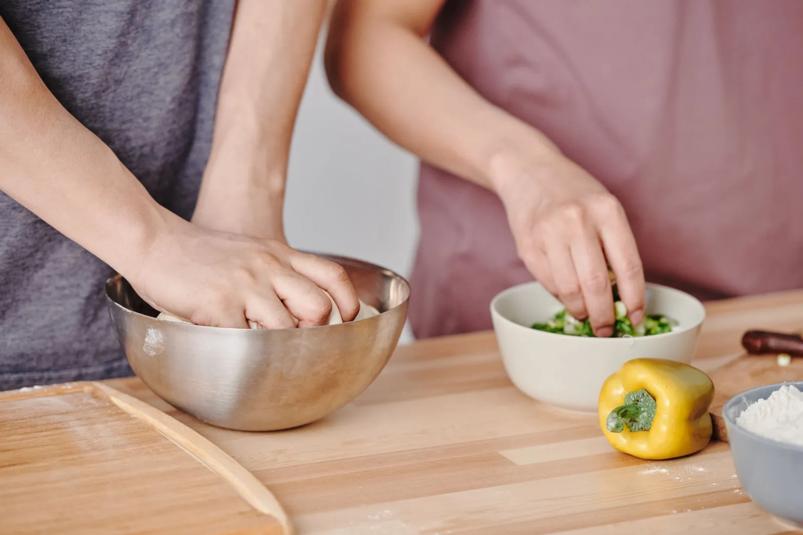 Two people preparing ingredients in bowls beside a yellow capsicum
