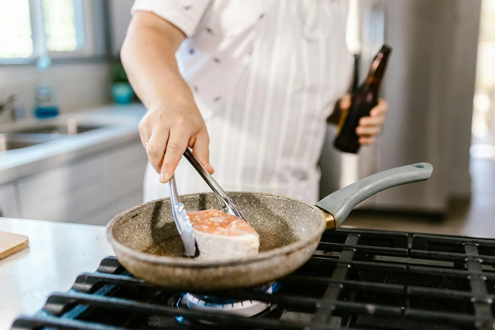 Person preparing a colorful nutrient-dense meal with salmon, leafy greens, and sweet potato in a bright kitchen