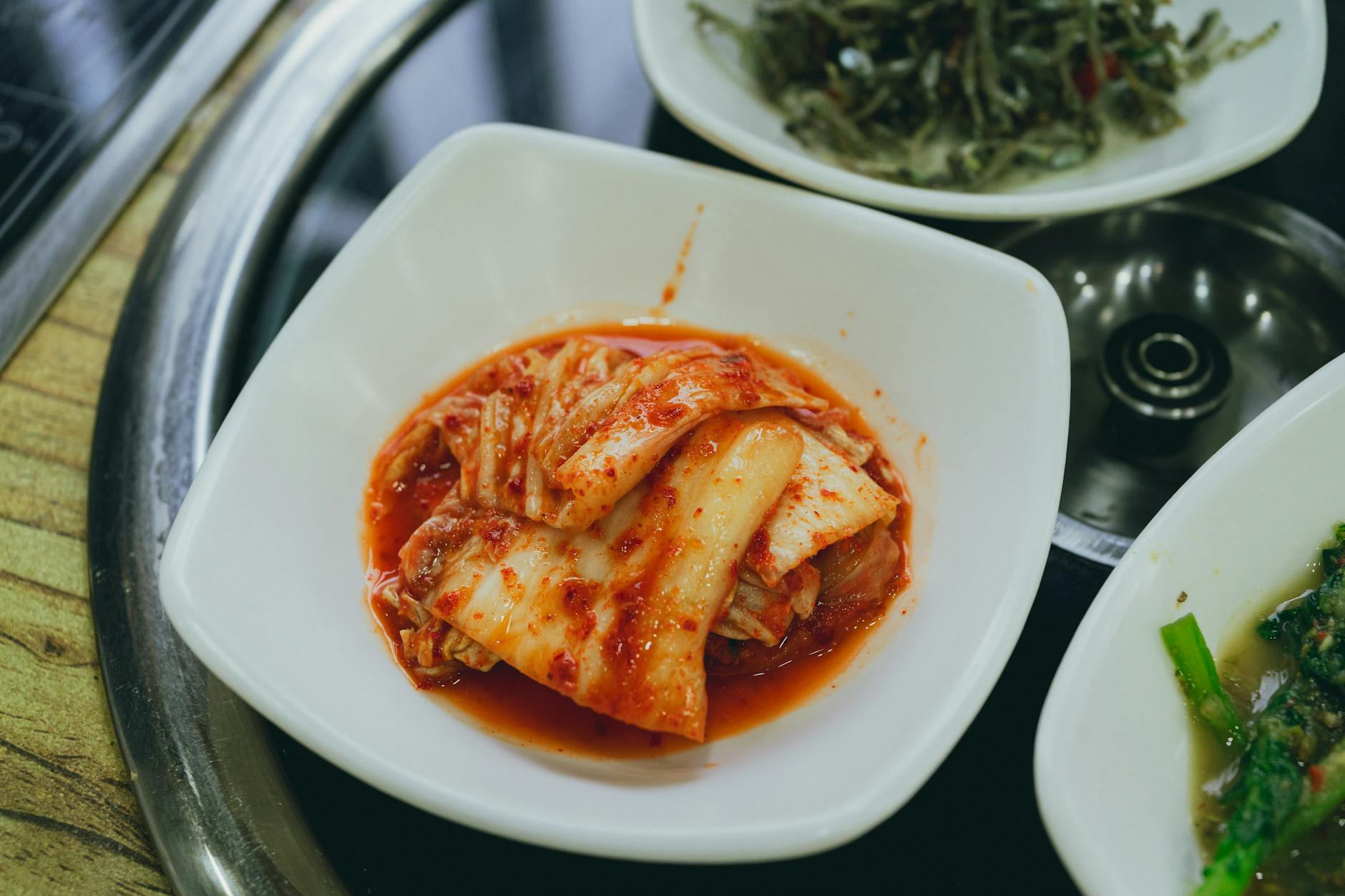 Bowls of gut-friendly fermented foods like yogurt and kimchi alongside salmon, walnuts, and leafy greens on a wooden table