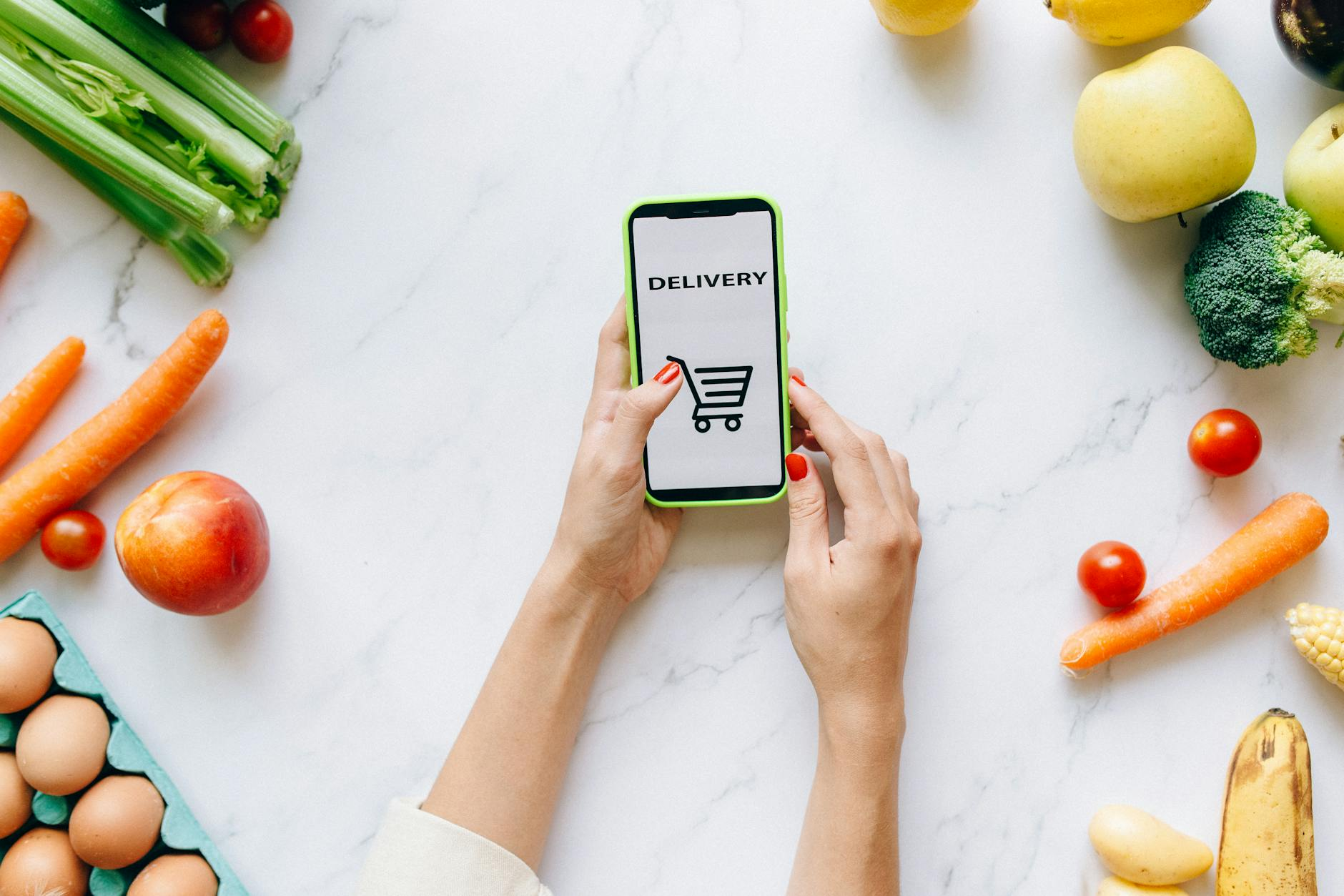 Person using a smartphone calorie tracking app while organizing weekly meal prep groceries in a bright kitchen