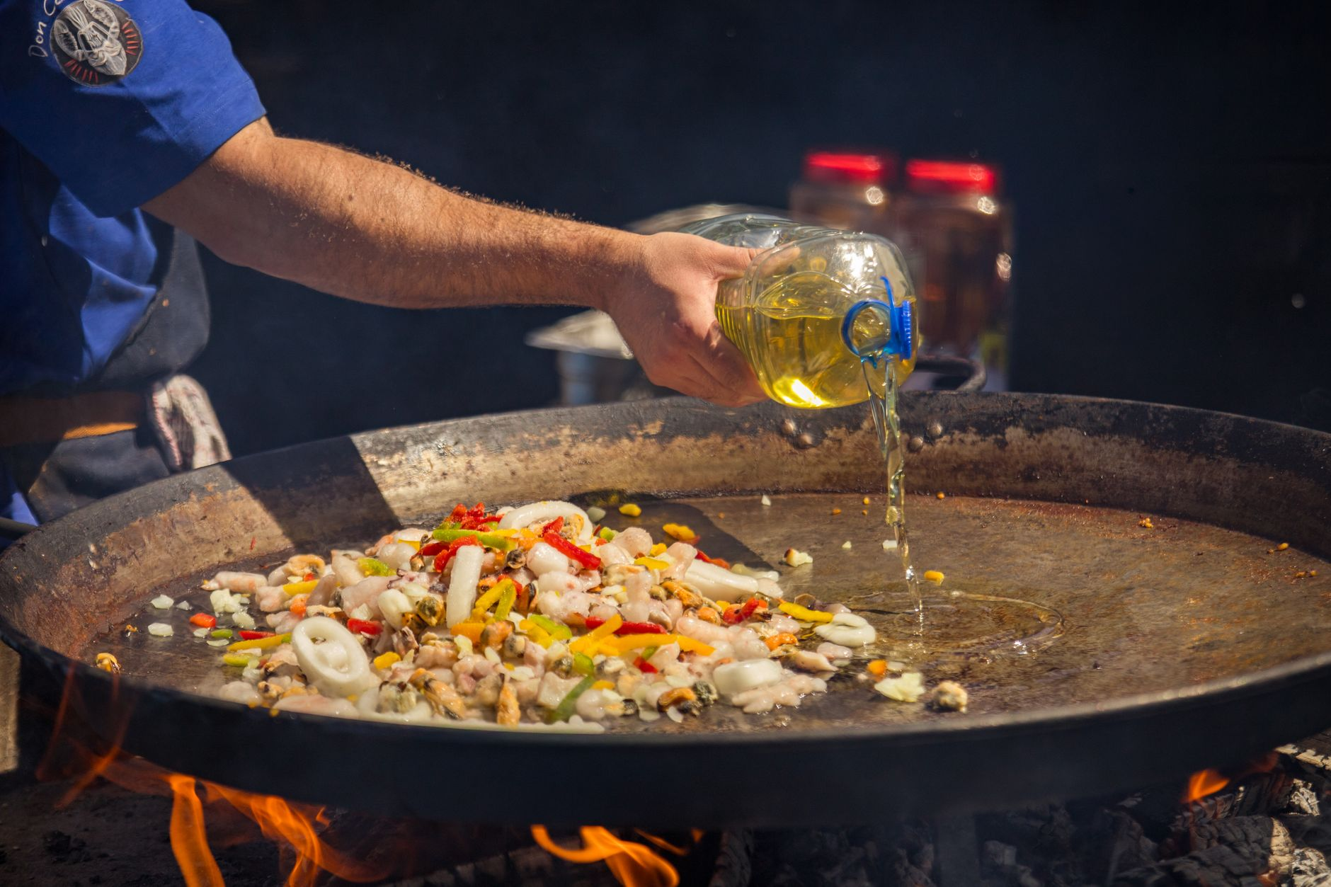 A digital kitchen scale weighing chopped vegetables beside a bottle of cooking oil being poured into a hot wok, with a smartphone showing a calorie tracking app on a sunlit kitchen counter