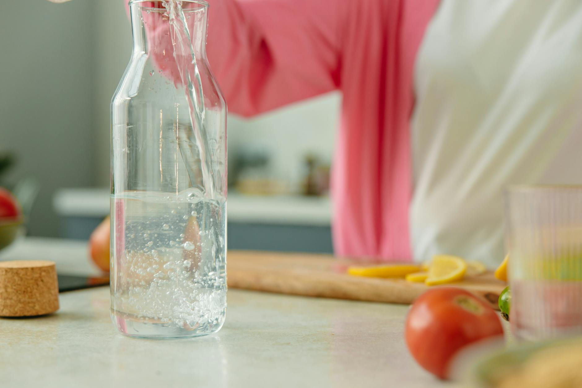 Glass of water poured before a meal on a kitchen counter with fresh vegetables and a notepad to track hydration