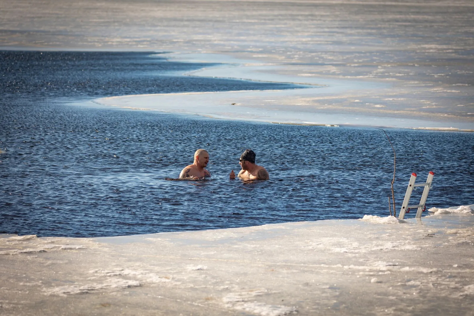 A person sitting in an outdoor ice bath barrel in cool morning light beside a towel and a smartphone showing a calorie tracking app, illustrating how few extra calories a typical cold plunge actually burns