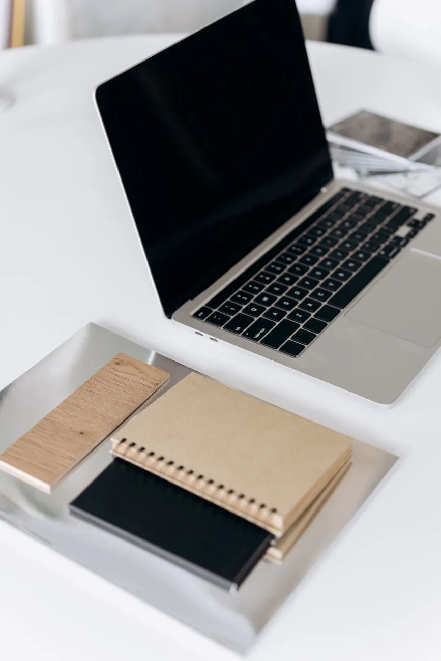 Notebooks beside a laptop on a white desk