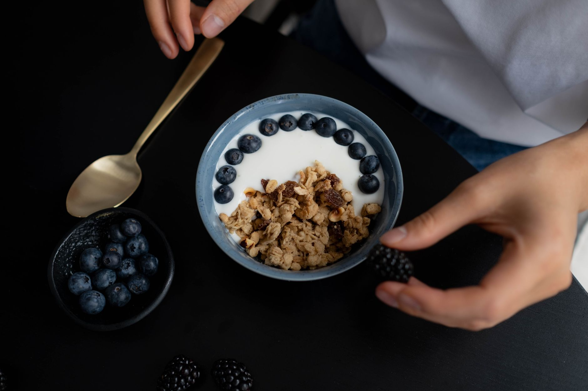 A smartwatch and a smart ring on a sunlit windowsill beside an open cycle-tracking journal, a glass of water, and a bowl of yoghurt and berries, illustrating menstrual-cycle calorie tracking