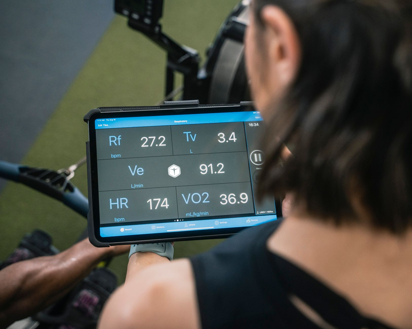 A printed 2024 Compendium of Physical Activities MET table beside a stopwatch, a chest-strap heart-rate monitor, and a smartphone showing calorie estimates on a sunlit gym bench