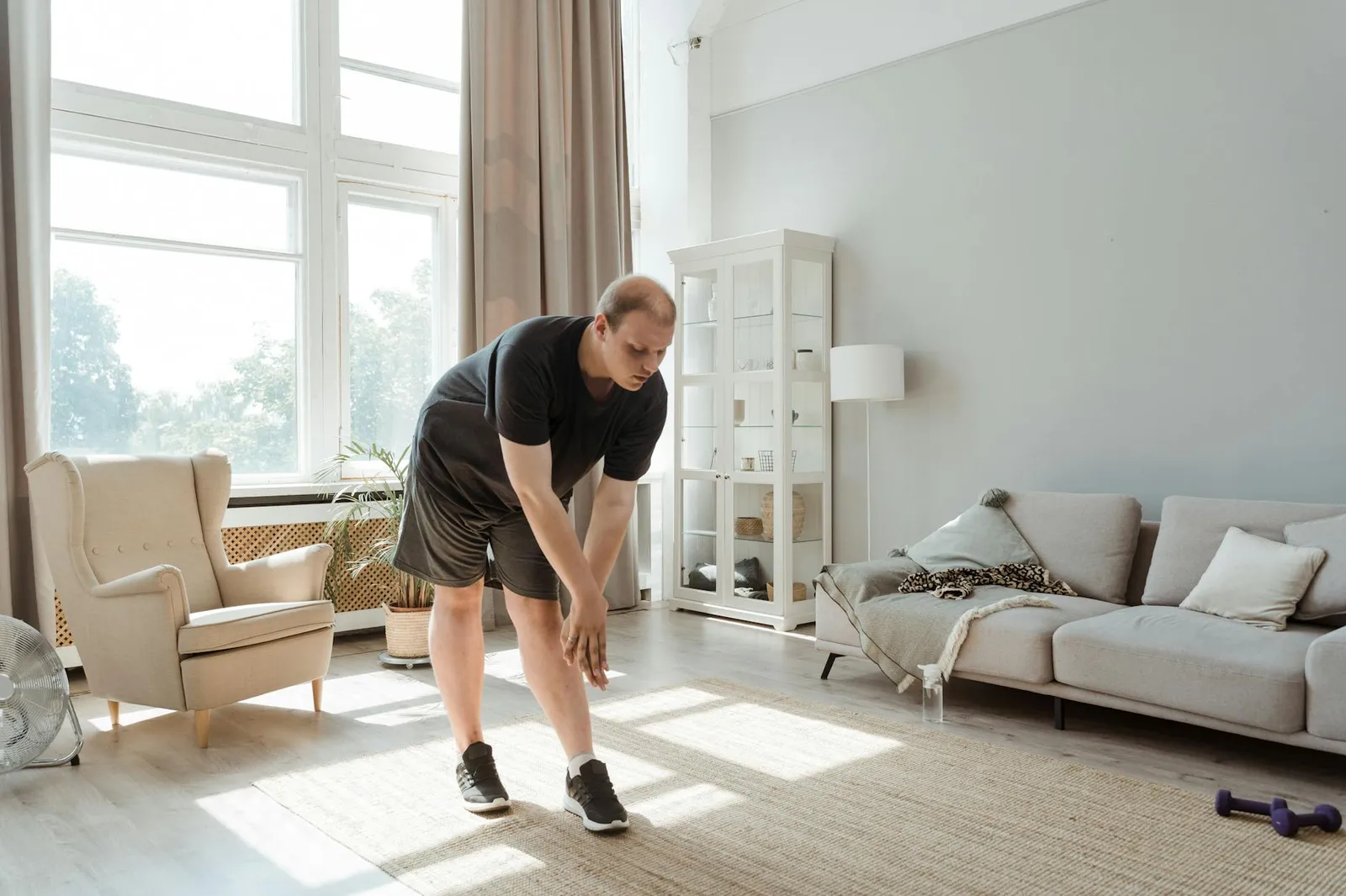 Person exercising and stretching in a living room with healthy food and a fitness tracker on a nearby table