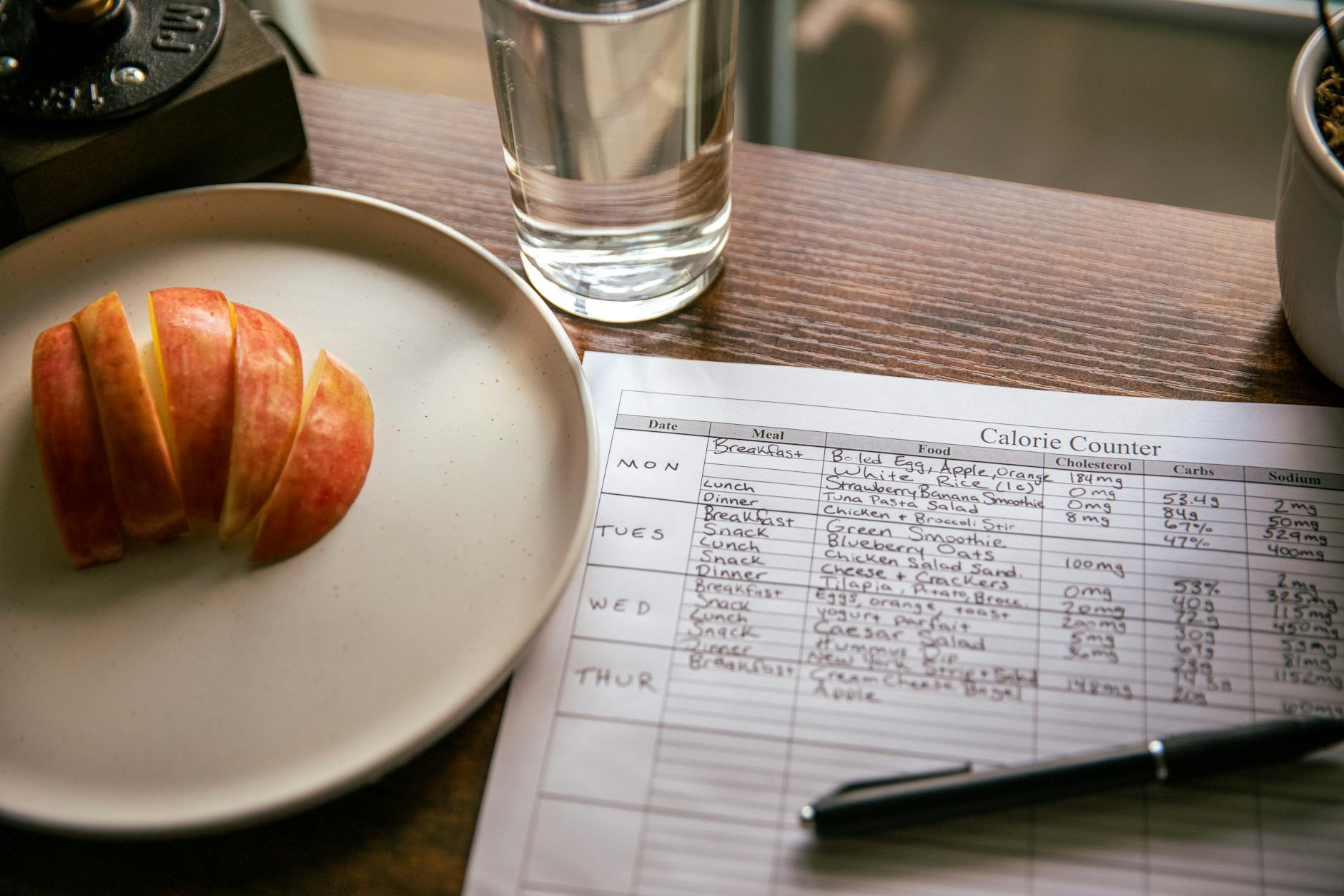 Person reviewing nutrition data and a meal plan at a kitchen table with a balanced meal and digital food scale nearby