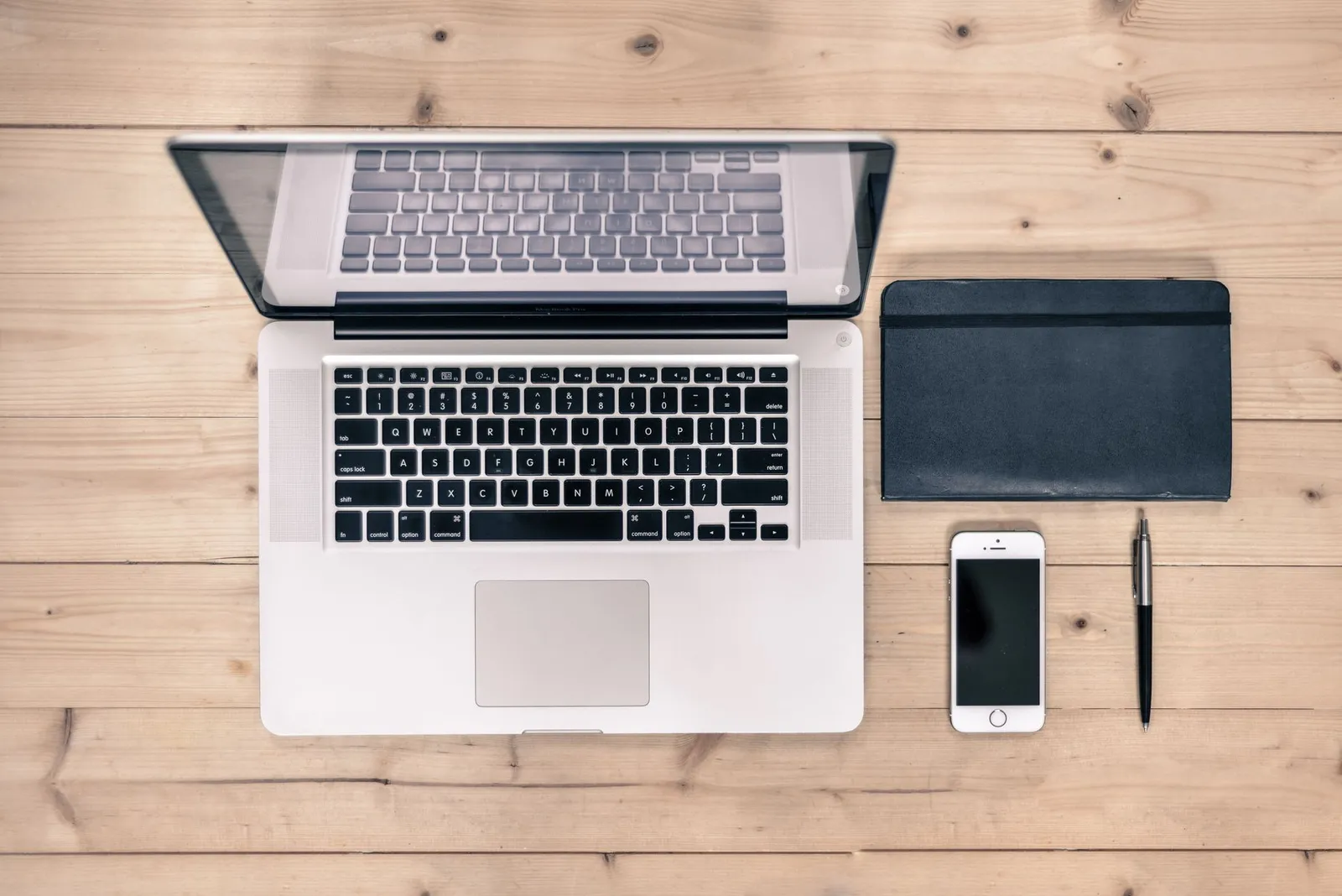 Laptop, black notebook, phone and pen on a wooden desk