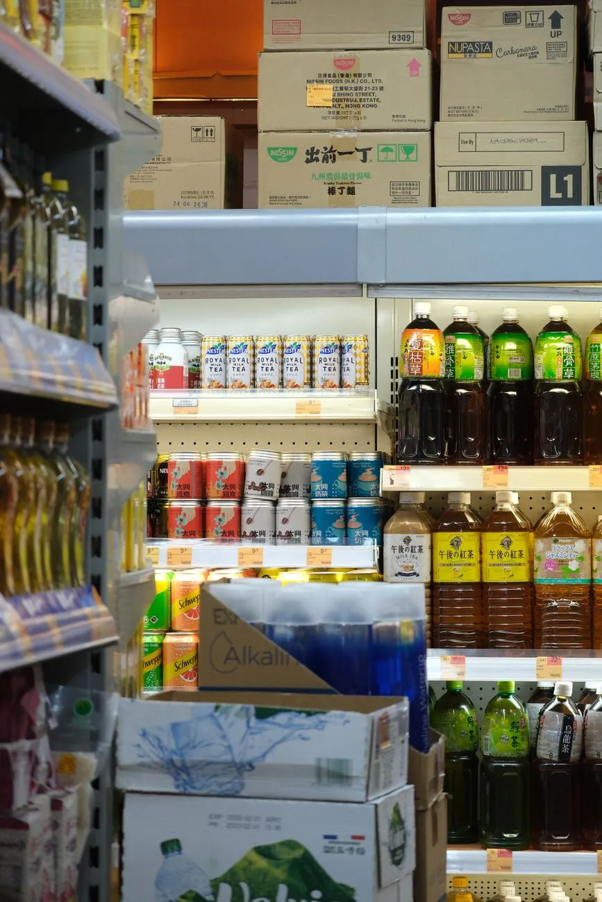 Bottled drinks and cans on supermarket shelves beneath stacked cartons