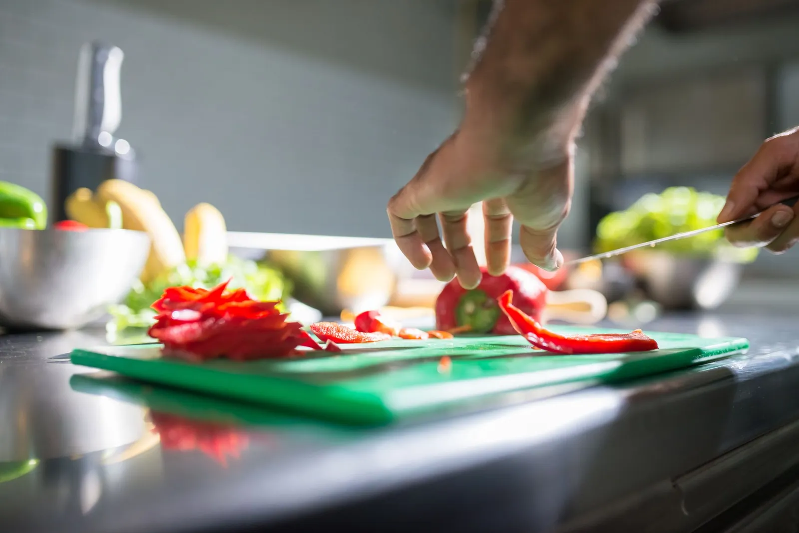 Hands slicing red capsicum on a green chopping board