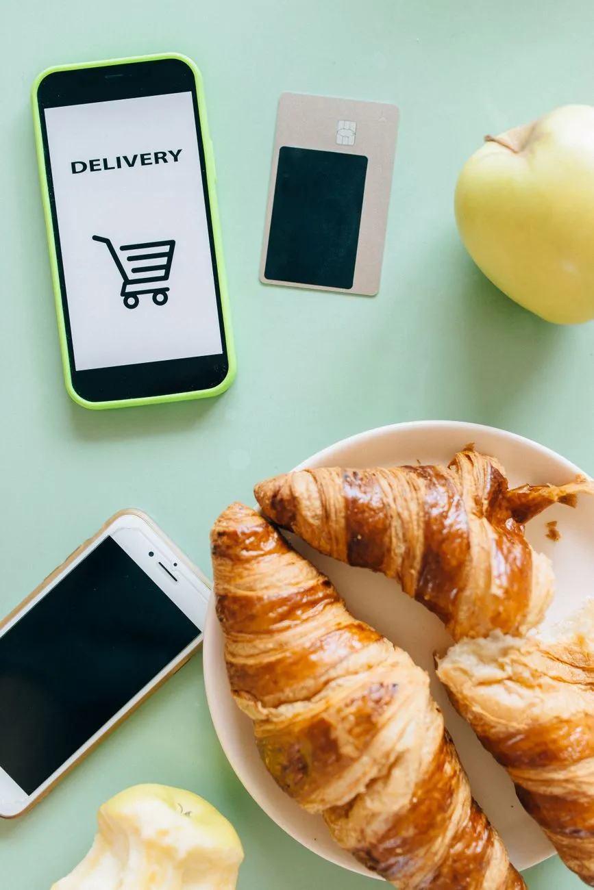 Smartphones beside croissants and apples on a table
