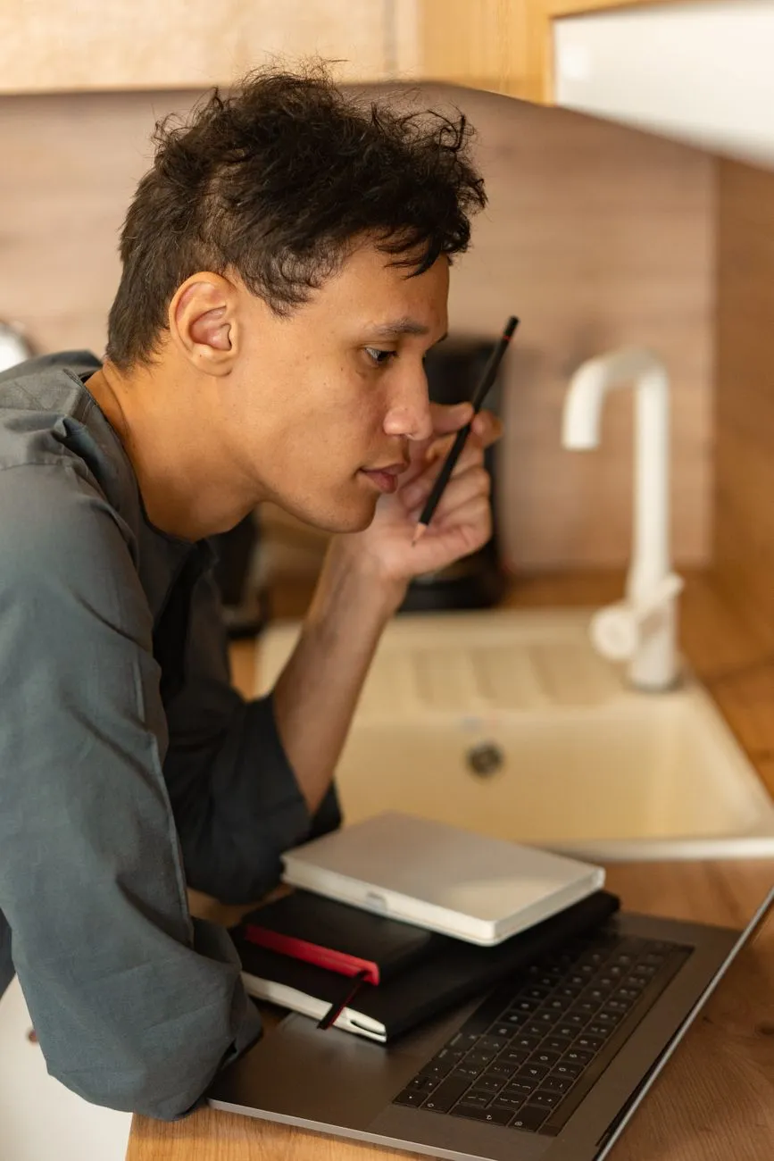 A person with a laptop and stacked notebooks at a kitchen counter