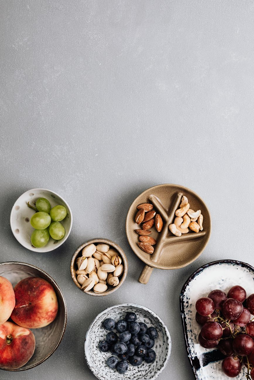 Small bowls of almonds, walnuts, cashews, and pistachios beside a printed table comparing labelled and measured calories on a sunlit kitchen counter, illustrating the per-nut gap between Atwater label values and absorbed energy