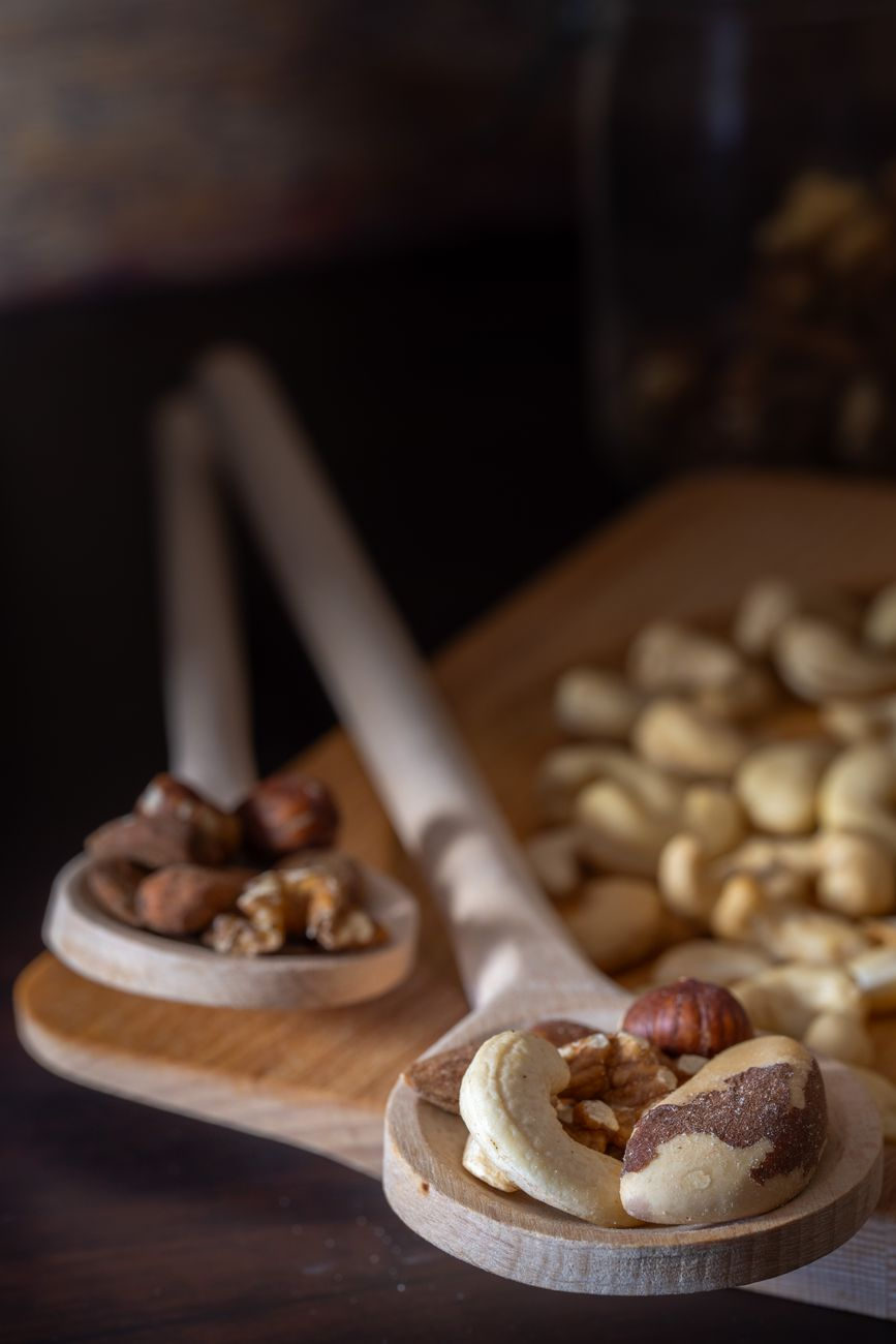 A jar of almond butter with a spoon beside whole and chopped almonds on a wooden board in a sunlit kitchen, illustrating how processing raises the calories your body absorbs from the same nut