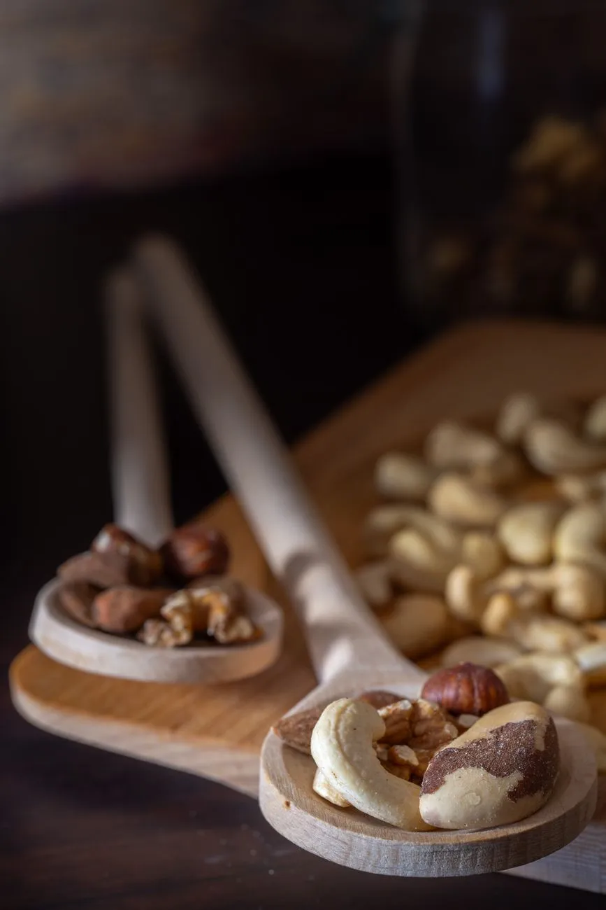 A jar of almond butter with a spoon beside whole and chopped almonds on a wooden board in a sunlit kitchen, illustrating how processing raises the calories your body absorbs from the same nut