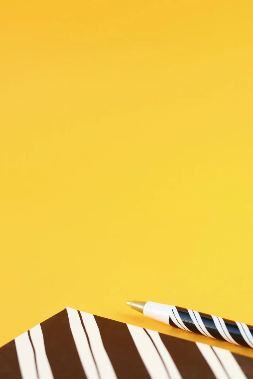 A striped notebook and pen on a yellow surface