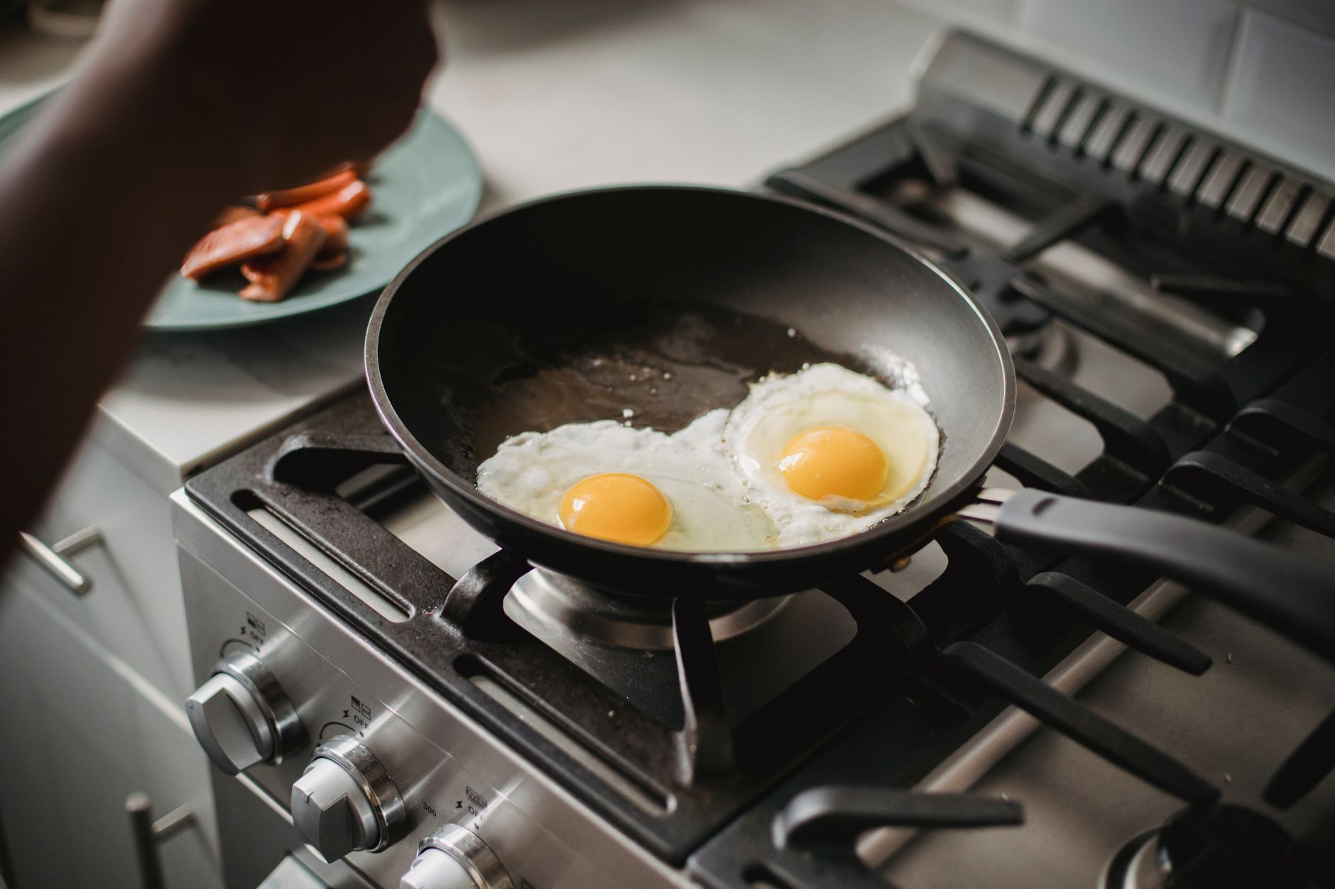 A plate of grilled chicken, eggs, and yoghurt beside a printed study summary and a calculator on a sunlit kitchen counter, illustrating the dose-response studies behind the 30 g protein per meal myth