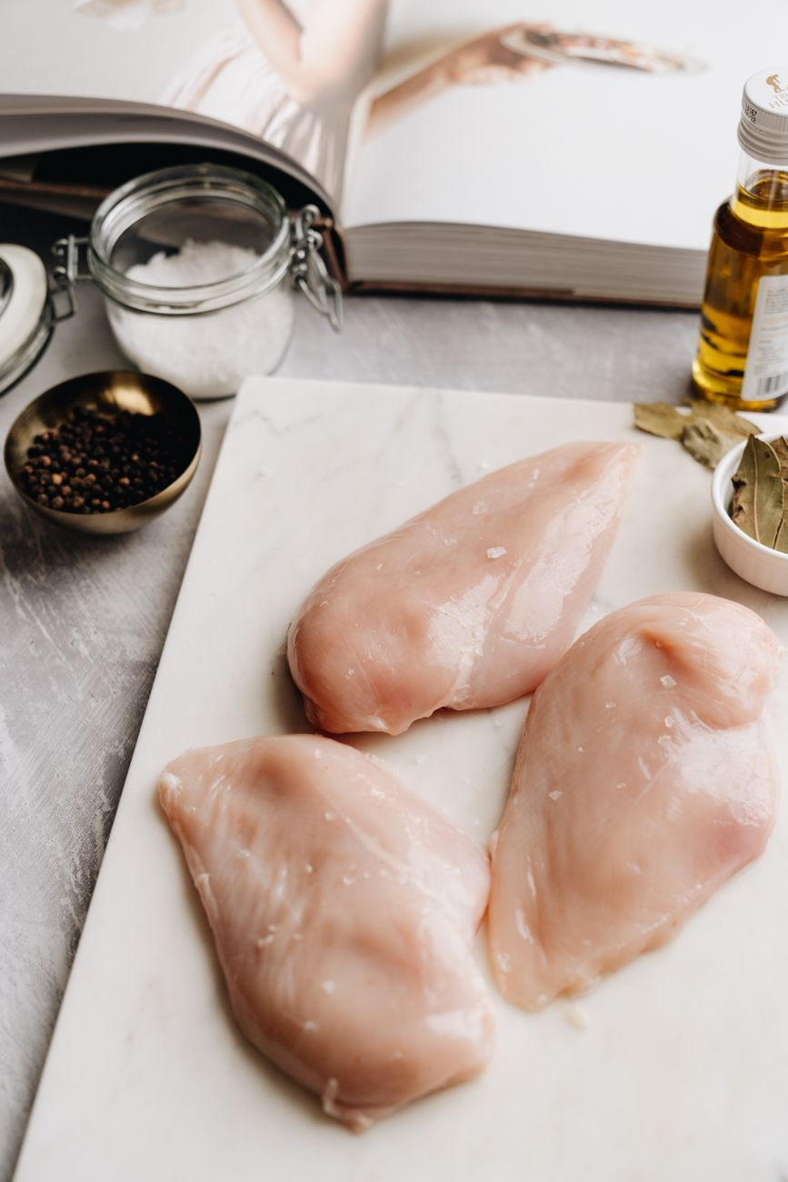 A protein shake beside a digital kitchen scale weighing chicken breast and a smartphone showing a protein tracking app on a sunlit kitchen bench, illustrating per-meal protein targets by body weight