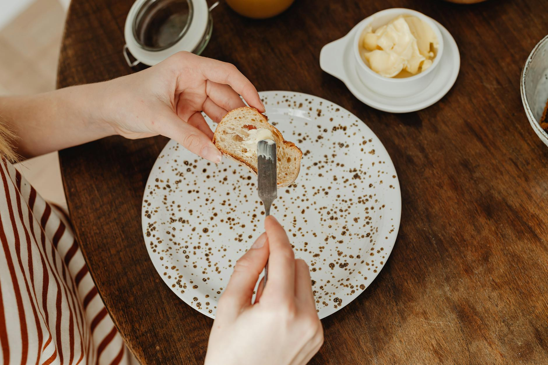 Person journaling at a calm kitchen table with a balanced breakfast and smartphone showing a nutrition app nearby