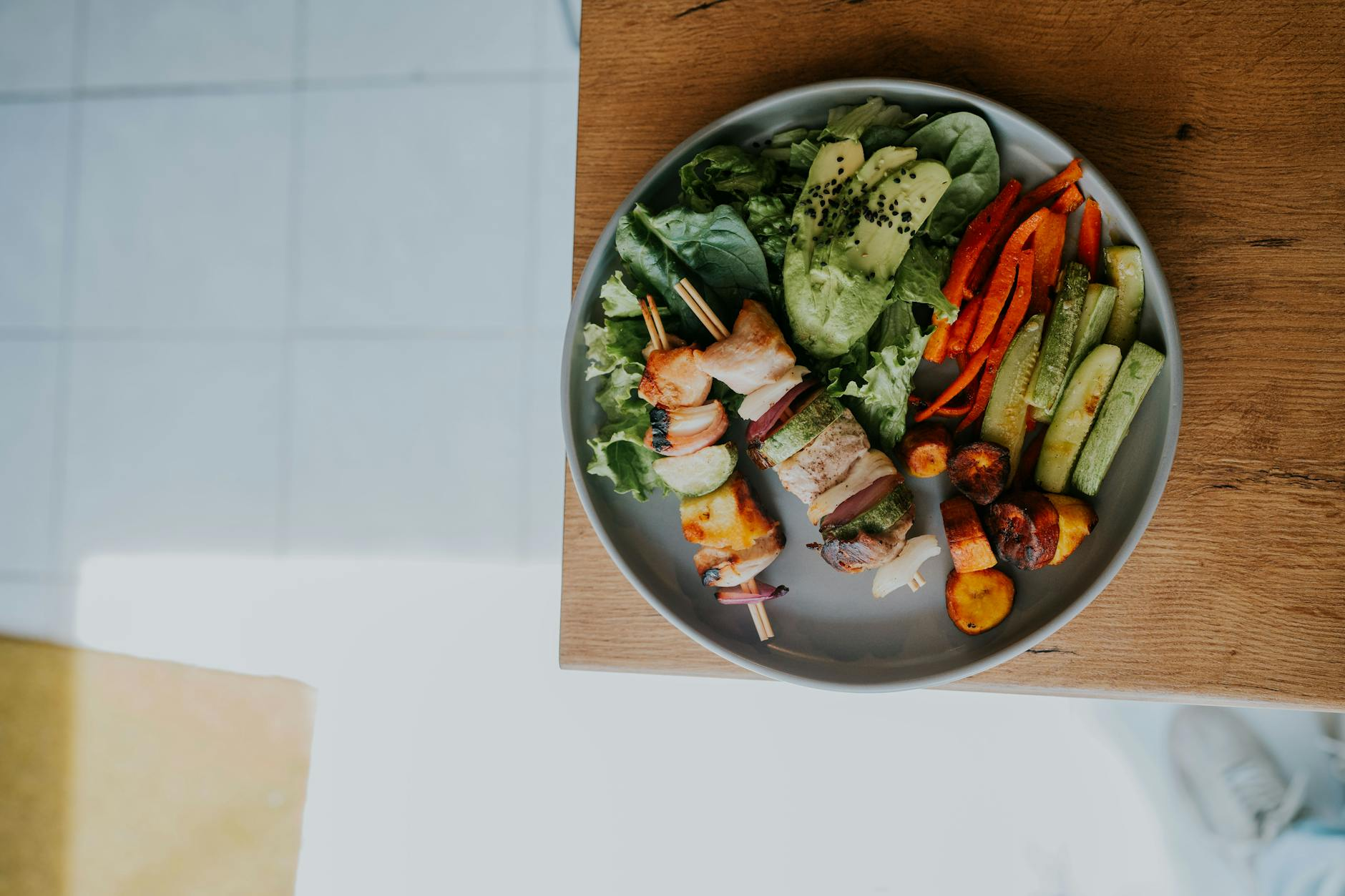 Balanced post-diet meal with grilled chicken, sweet potato, vegetables, and avocado on a kitchen counter alongside a notepad showing weekly calorie targets