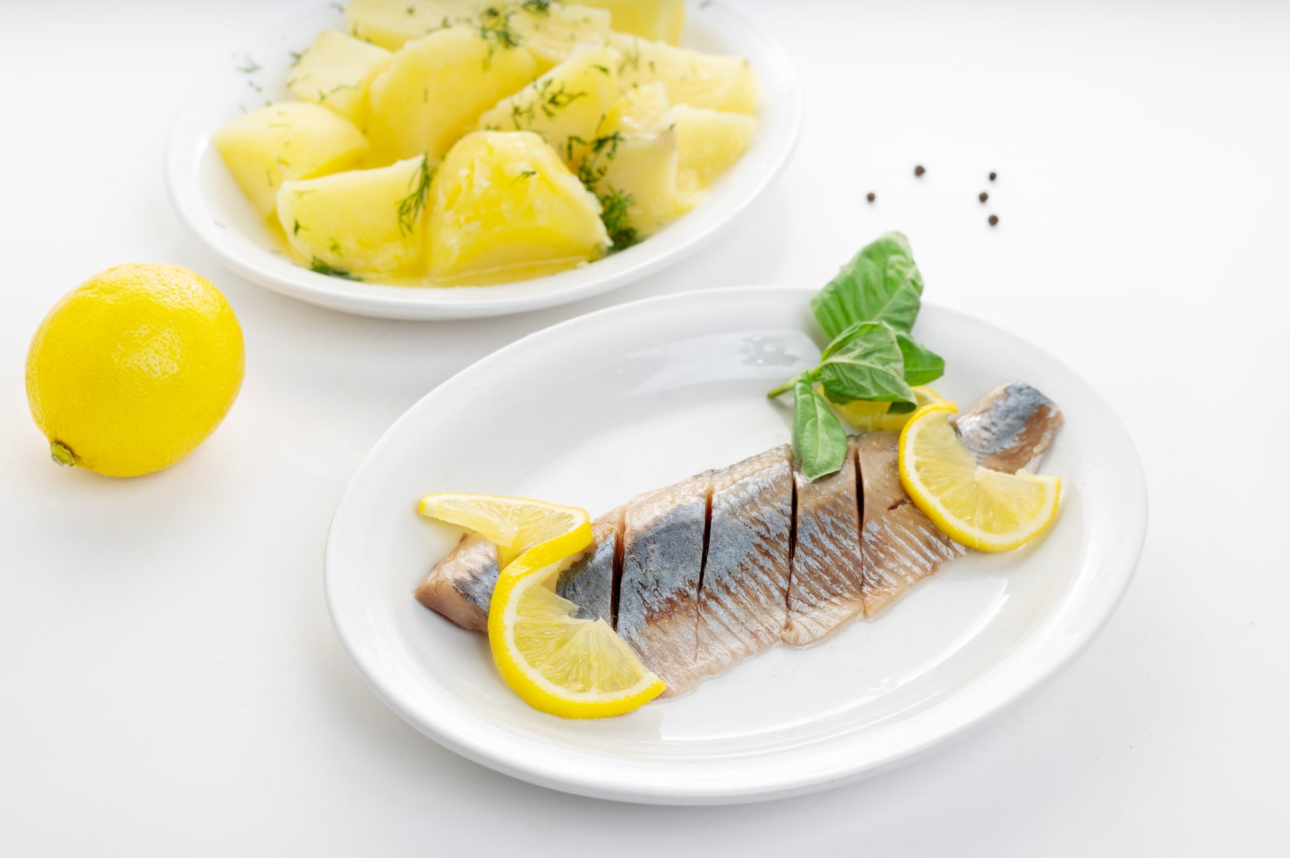 A bowl of boiled potatoes beside a plate of grilled fish, a bowl of porridge, fresh oranges and apples, and a smartphone showing a calorie tracking app on a sunlit kitchen counter, illustrating the foods that rank highest on the satiety index per calorie
