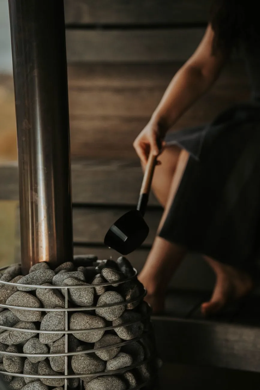 A person holding a ladle over hot sauna stones