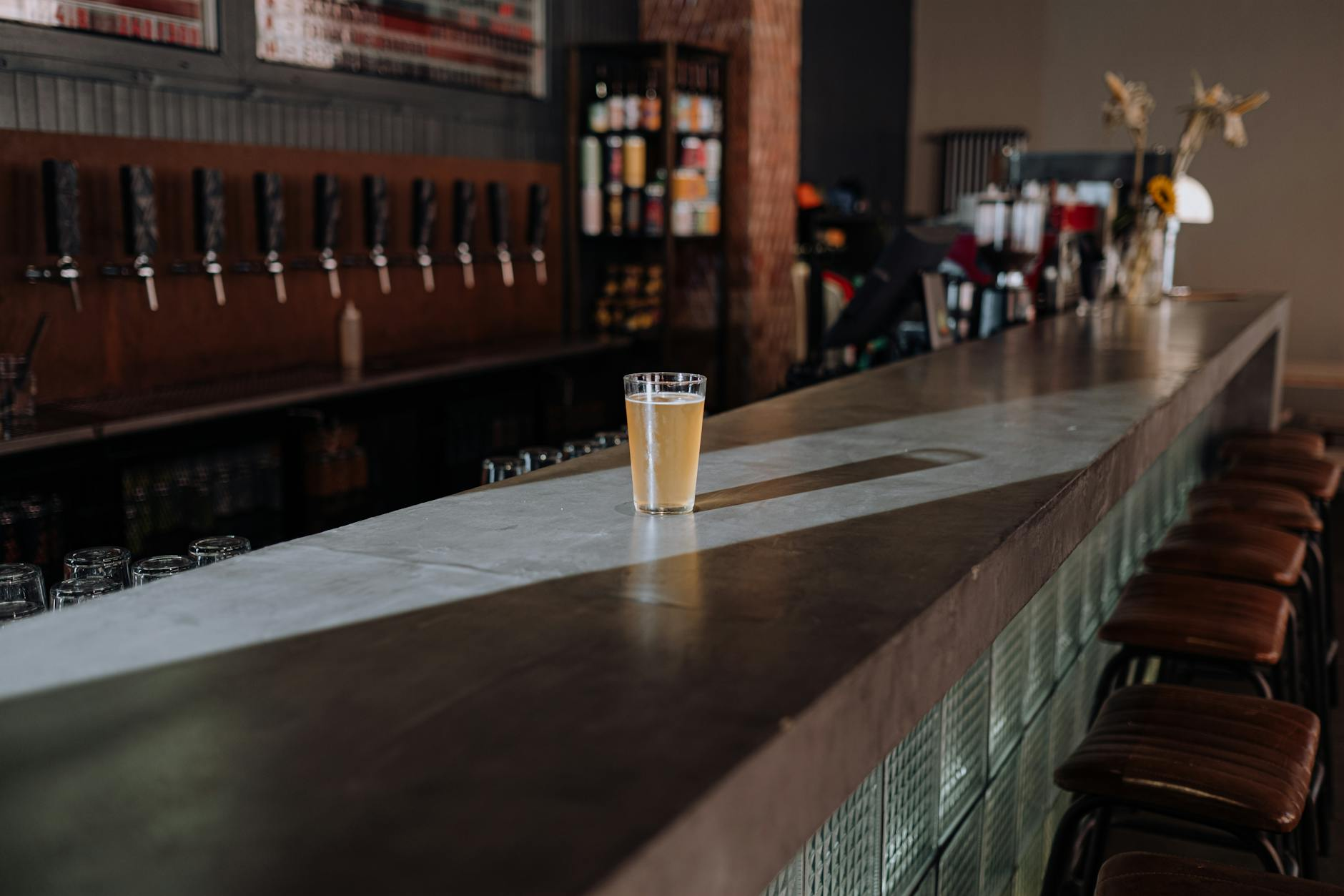 Four Australian beer glasses lined up on a wooden bar counter — a 285 mL pot, a 425 mL schooner, a 570 mL pint, and a smaller middy — each filled with golden beer beside a small chalkboard listing kilojoules per glass