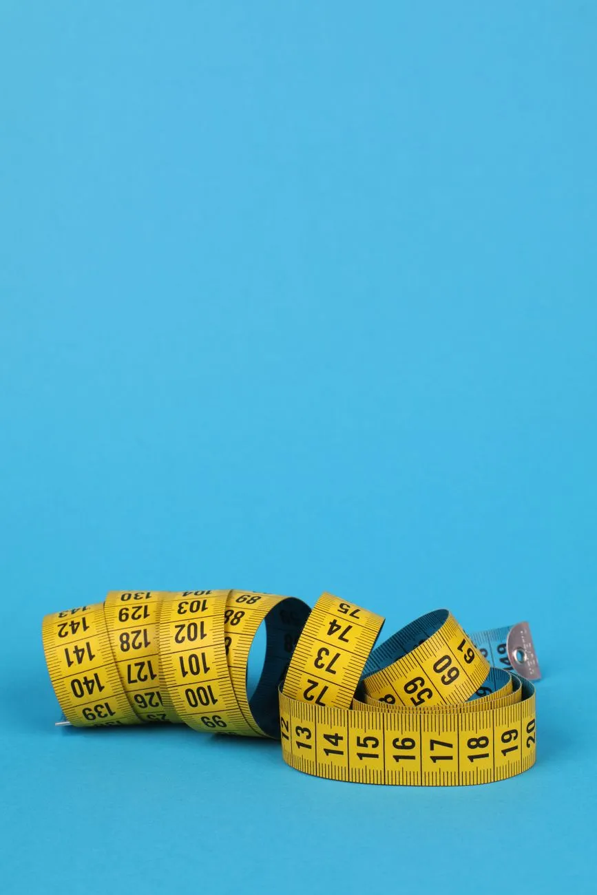A smart bathroom scale beside a printed table comparing body fat readings from consumer scales with DXA results, a calculator, and a tape measure on a sunlit bathroom floor, illustrating the per-device error ranges found in validation studies