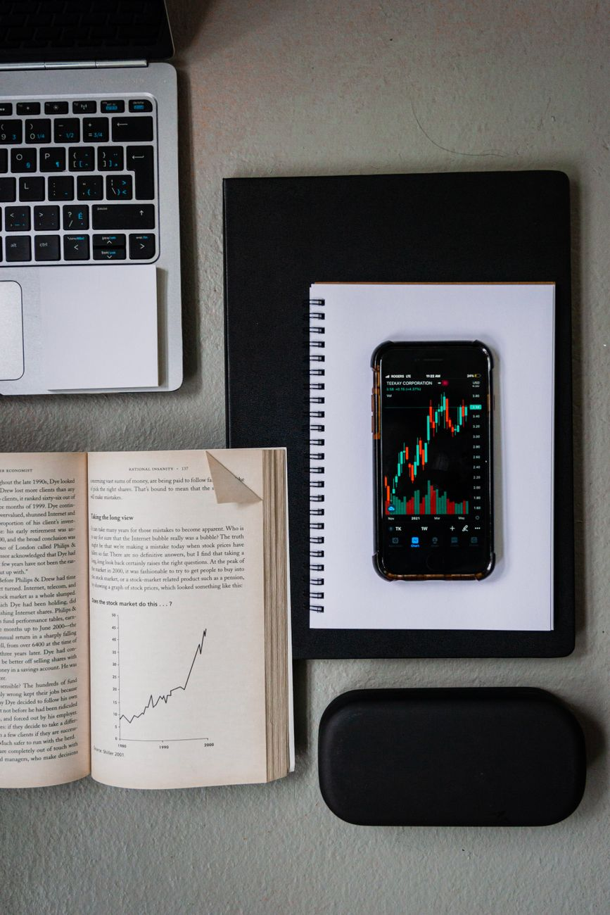 An open notebook showing a hand-drawn body fat trend line smoothing out daily readings, beside a smart scale and a smartphone with a body composition graph in soft morning light, illustrating why the trend is more trustworthy than any single reading