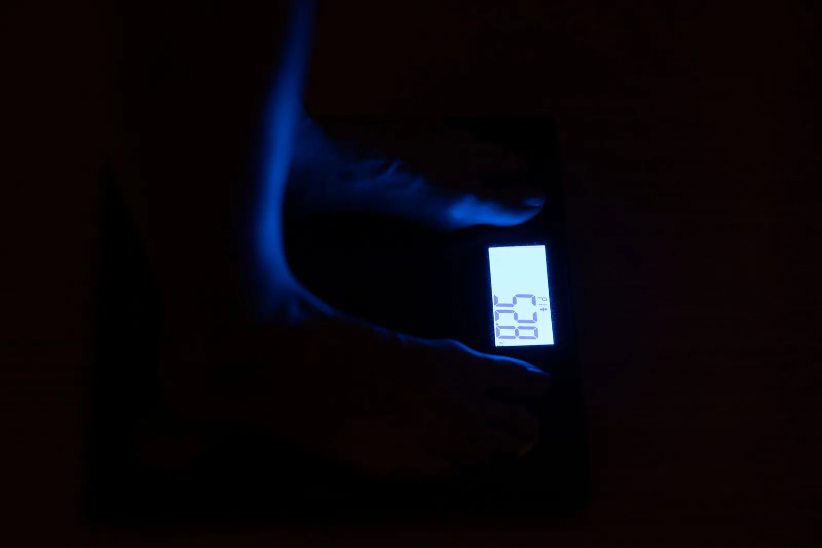 A smart bathroom scale showing a body fat percentage reading beside a smartphone with a body composition graph, a tape measure, and a glass of water on a sunlit bathroom floor, illustrating how smart scale body fat estimates compare with DXA laboratory measurement