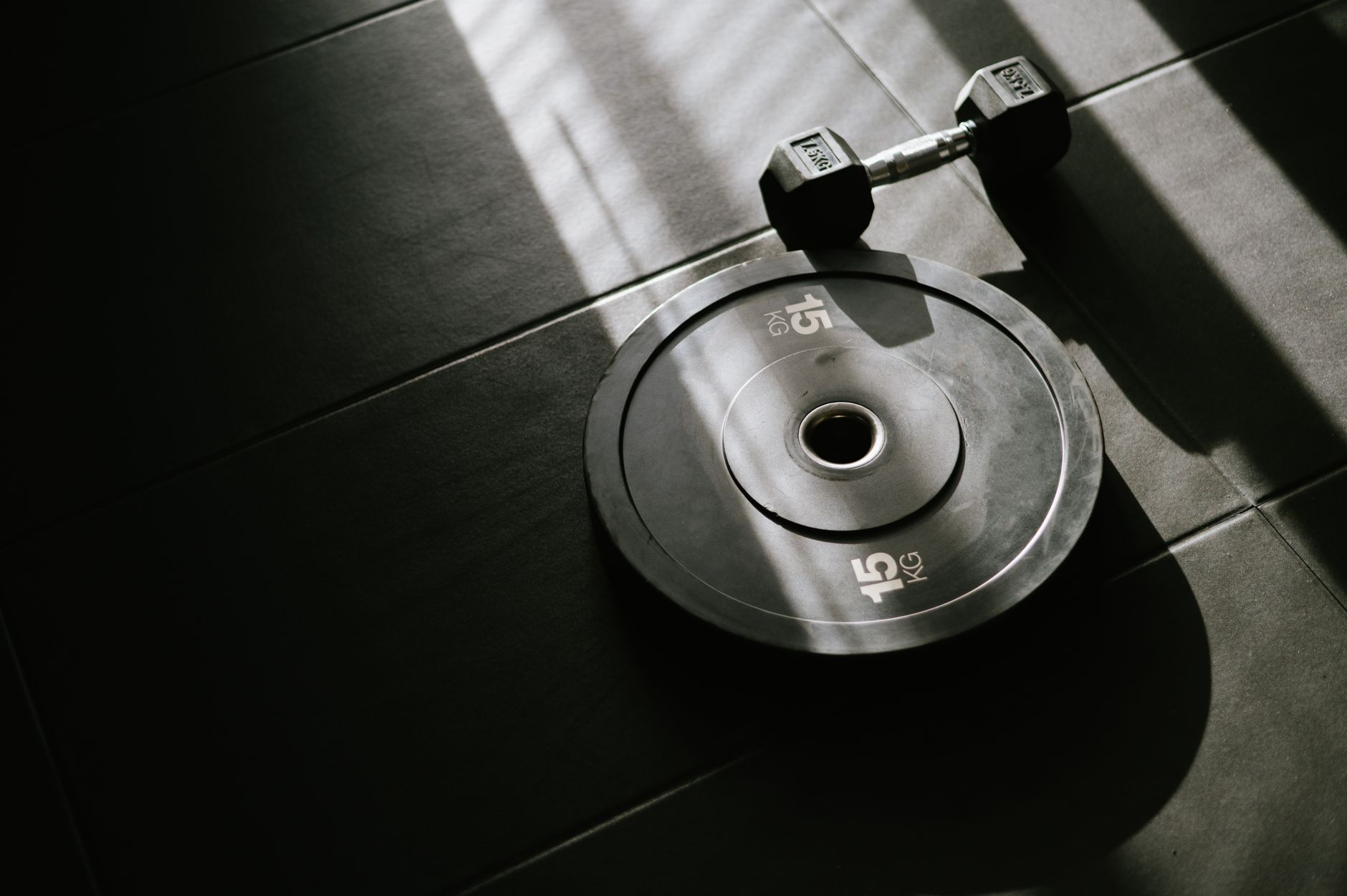 A dumbbell and barbell on a gym floor beside a smartwatch showing a calorie-burn number and a smartphone with a calorie tracking app in a sunlit gym, illustrating how strength-training calories are estimated